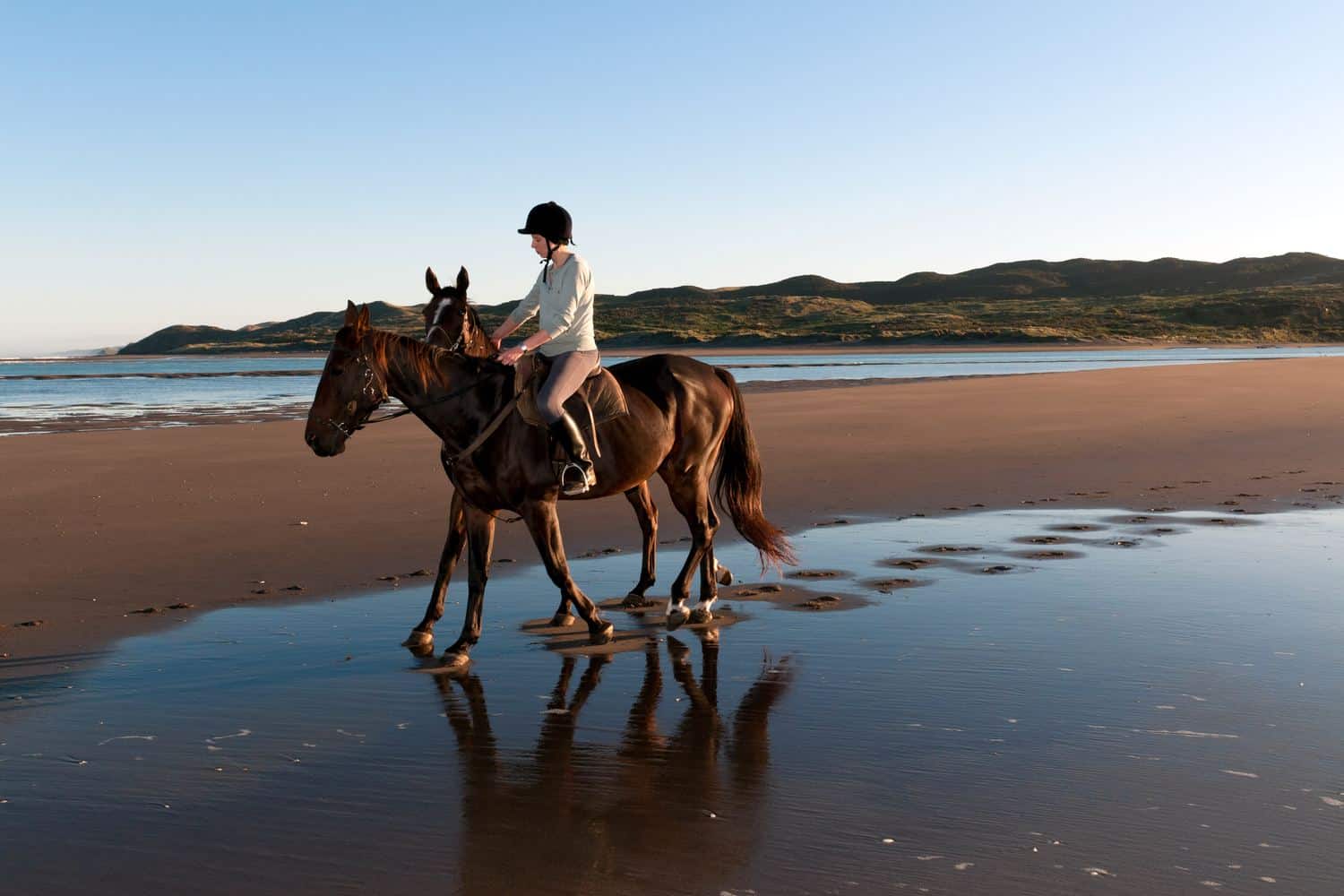 Cavalière en balade à cheval sur une plage de sable à marée basse